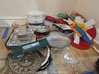 Full view of assorted kitchenware and bakeware including Pyrex, Corning Cornflower dishes, plastic containers, metal trivets, and graters.