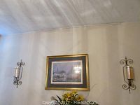 Photo showing the two iron wall sconces with glass candle holders mounted on the wall with the framed print centered between them.