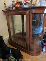 Front and side angled view of glass and wood curio cabinet with rounded edges, showing the single front door and glass panels on sides.