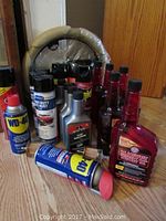 Car care products arranged on floor including six Marvel Mystery Oil bottles (red), three Motor Medic Lead Substitute bottles (silver with red caps), two Eastwood Anti-Rust and More cans and two WD-40 spray cans.