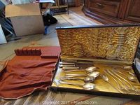 Wide view of all flatware pieces laid inside an open fitted case with satin lining and a cloth carrying pouch beside it.