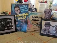 Group photo of four framed Humphrey Bogart items including two posters, one photograph and one art print on a surface.