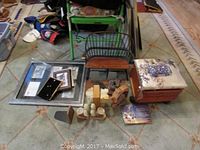 Overall view of decorative items including wooden doll bench, bookends, framed artwork, cushioned stool, and figurines arranged on floor.