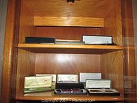 Wooden shelf with eleven pen sets boxed, some with visible brand names like Cross and Saint Laurent.