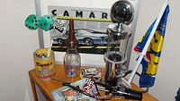The lot as shown with the Camaro poster in the background and various collectibles on a small chest including gas pump drink dispenser, dice, mug and cup with racing flags.