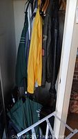 Men's jackets hanging on hangers including a yellow jacket, a leather bomber jacket, and others. Several umbrellas at bottom.