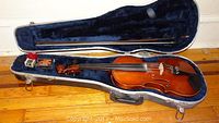 Violin, bow, and case with plush blue interior shown fully open on wooden floor.