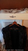 Black faux fur coat hanging on a wooden hanger
