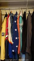 Full view of eight men's jackets hanging side by side. Varied colors including yellow, red, blue with stars, orange, teal, black, and brown. Several jackets show brand or racing patches.
