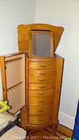 Front view of oak jewelry cabinet with hinged mirror open and left side door open showing necklace hooks.