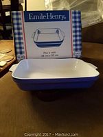 Photo of Emile Henry rectangular baking dish with original packaging showing model and size (38x30 cm). Dish has white interior and burgundy exterior.