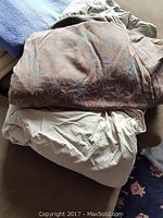 Image showing a twin down comforter in a light solid color partially covered by a decorative cover featuring palm tree patterns in muted tones.