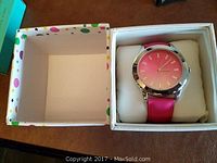 Open box showing pink watch secured on a white cushion inside a white box with multicolored polka dots.