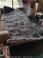 Grey shag carpet laid partially folded on a couch, showing the shaggy texture and size.