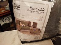 Photo shows packaging of Home & Dorm reversible furniture protector for sofas up to 96 inches wide with usage example of child and dog on sofa.