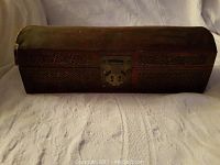 Front view of closed vintage opium box showing carved wood design and metal latch.