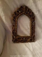 Photo of the ornate wooden frame with floral and leaf carvings, displayed on a white fabric background.