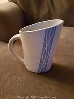 Ceramic milk jug with blue and gray vertical stripe, held upright on a fabric surface.
