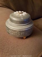 Top and side view showing circular metal body and decorative embossed design on top.