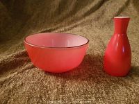 Photo of the pink pearl glass bowl with a gold rim alongside the small red vase on a brown textured background.