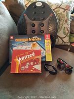 Photo showing Yahtzee and Words with Friends board games, three sunglasses, and Dr. Ho backrest on a sofa.