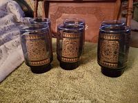 Group of six blue vintage glasses showing intricate gold motif designs around the sides, arranged in two clusters.