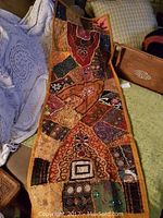 Full view of large orange wall hanging with colorful embroidery and patchwork designs laid out on a wooden chest, showing detailed patterns and texture.