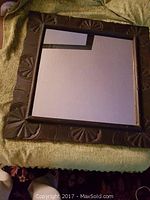 Full view of 27x27 inch square mirror with dark carved wooden frame displaying Balinese motifs.