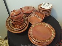 A group shot of Mexican pottery dishes consisting of plates stacked, small covered bowls in a pile, a large covered serving bowl, and a square shallow dish, all decorated with white and green floral and dot patterns on terracotta clay.