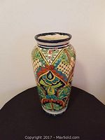 Front view of the hand-painted Mexican ceramic urn on a black cloth surface showing floral and geometric decorative patterns.