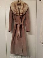 Full view of the long suede jacket with fur collar hanging on a hanger showing the full front profile with belt tied around the waist.