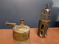 Photo of two antique lanterns, one brass wick lantern and one metal cage lantern with hook.