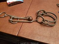 Photo of antique metal puzzle showing two linked rings connected by a chain to a large metal hook and ring detail.
