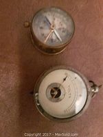 Top view of a brass antique compass and a round voltage meter with visible dials and needles.