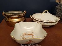 Photo showing brass lion figurine, covered porcelain dish, and porcelain bowl together on a surface