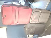 Three large suitcases in red, beige, and black colors, standing upright showing front pockets and wheels on a tiled floor.