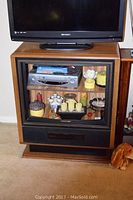 Front view of the refurbished TV stand with a flat screen TV on top and glass cabinet below showing contents inside.