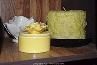 Photo of yellow round candle with rose top, textured pillar candle, and empty white lotus candle holder on wooden shelf