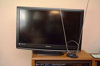 Front view of Emerson LCD TV on a stand with Polaroid antenna placed next to it, showing screen and general condition.