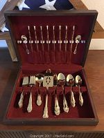 Full 8 piece serving flatware set by Korea Rogers displayed in open wooden box with red velvet lining, showing detailed ornamental handles and including serving forks, spoons, and pierced spatula.