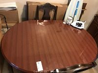 Top view of wooden oval dining table with polished reddish-brown finish and Queen Anne style backrest chair visible.