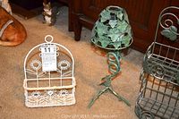 Photo of white sunflower wall shelf, green metal candle holder, and part of green metal basket on beige carpet in front of wooden cabinet