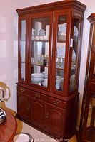 Front view of the two-piece china hutch with glass doors displaying dinnerware inside, showing the upper glass doors and lower wood cabinet with drawers.