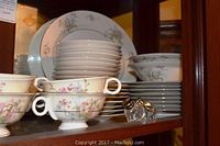Stacked dinner plates, bowls, cups with apple blossom floral pattern, and salt and pepper shakers.