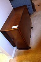 Side view of the drop leaf table showing closed leaves, wooden grain and side knob.