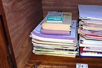 Stack of music books with box of music flash cards on top, beside a stack of assorted sheet music and a folder of blank music sheets.
