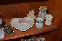 Shelf with various angel figurines, glass snow globe, decorative heart-shaped dish, and a small metal candle holder