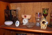 Shelf with an assortment of decorative items including plaques, glassware, teacups, and a floral scale clock.