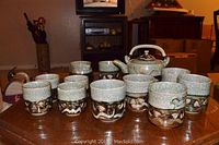 Full view of all tea set pieces: nine tea cups, creamer, sugar bowl, and teapot on wooden table.