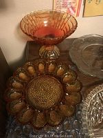 Photo shows pink pedestal bowl with woven pattern, amber carnival glass plate with hobnail scalloped petals, and part of silver pedestal vase.